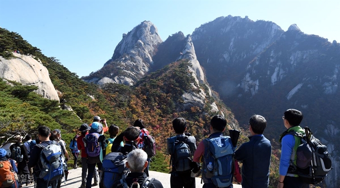 정상에 오른 등산객들이 북한산 숨은 벽 아래 단풍이 절정을 이룬 광경을 사진에 담고 있으며 가을 정취를 만끽하고 있다.