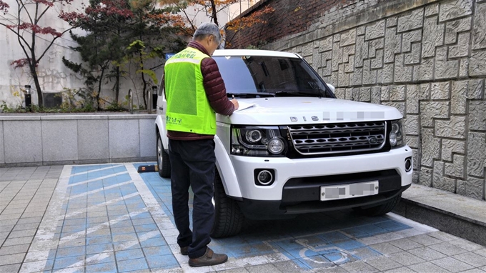 12일 강남구청 관계자가 논현동의 한 건물 주차장에서 비장애인 차량의 장애인전용주차구역 불법주차를 적발해 주차위반사실통보서를 붙이고 있다. 이한호 기자