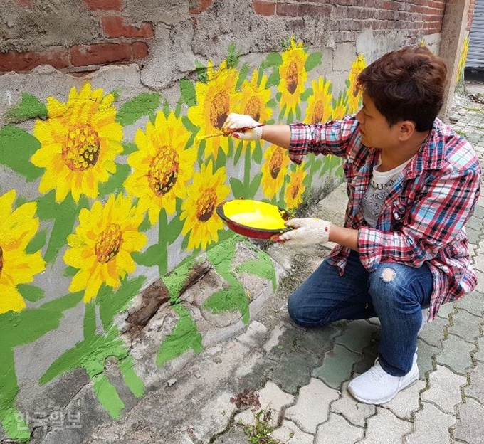 [저작권 한국일보]카페로 들어오는 바깥 골목부터 해바라기들이 손님을 맞이한다. 벽화를 그리고 있는 권 대표. 김윤곤기자 seoum@hankookilbo.com