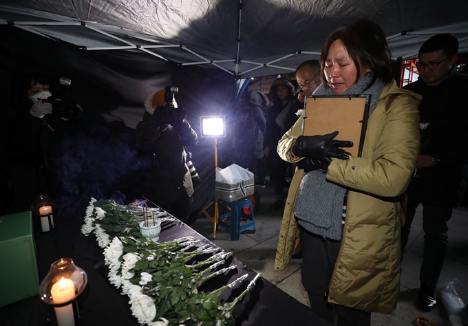 13일 태안화력발전소에서 비정규직으로 일하다 숨진 김용균 씨의 분향소가 마련된 서울 광화문광장에서 한 추모객이 영정을 쓰다듬으며 눈물을 흘리고 있다. 연합뉴스