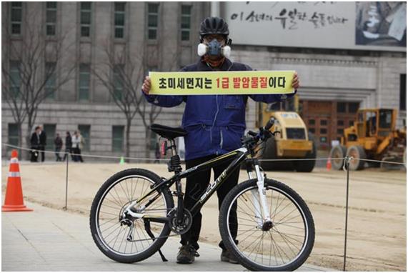 환경보건시민센터 한 활동가가 서울 시청 앞에서 방독면을 쓴 채 ‘초미세먼지는 1급 발암물질이다’라는 손현수막을 들고 있다. 환경보건시민센터 제공