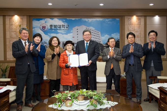 신언임(왼쪽에서 네번째)할머니가 26일 김수갑(왼쪽에서 다섯번째)충북대 총장을 찾아 8억원을 기탁하겠다는 뜻을 밝혔다. 대학 관계자들이 박수를 치는 가운데 두 사람이 기탁 약정서를 맞들고 있다. 충북대 제공