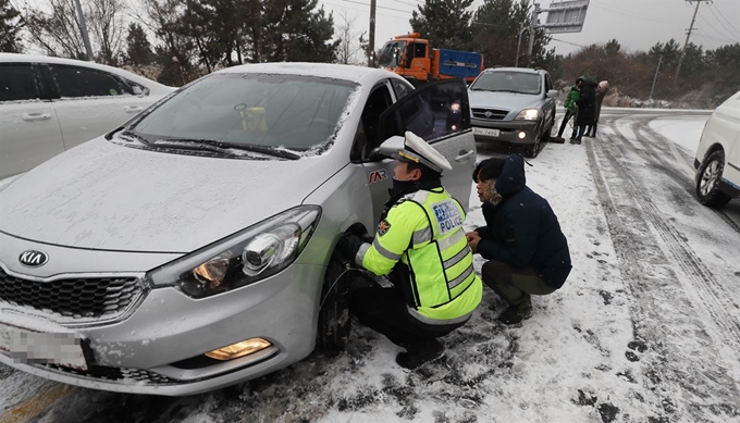 제주 산지에 대설주의보가 내려진 28일 오전 제주 산간도로에 대한 차량통제가 이뤄지자 어승생 삼거리 입구에서 자치경찰이 차량에 체인을 부착하는 운전자들을 돕고 있다. 연합뉴스