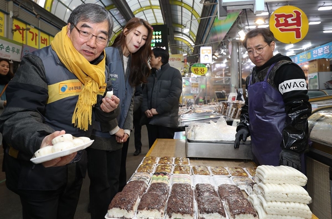 윤석헌 금융감독원장(왼쪽)이 23일 서울 양천구 신영시장을 찾아 나눔 행사에 쓰일 떡을 고르고 있다. 윤 원장은 금감원 공공기관 미지정 조건으로 기획재정부가 제시한 간부급 인력 감축 조건을 수용할 의사를 밝혔다. 연합뉴스