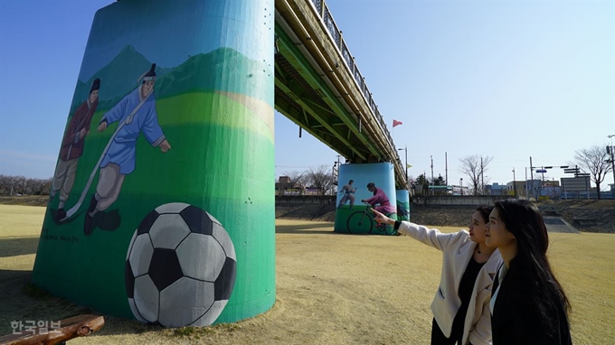 관광객들이 12일 경주시 성건동 형산강지류인 서천 장군교 교각 앞에서 신라 화랑이 축구하는 모습을 감상하고 있다. 경주시는 최근 폐철도교인 장군교 교각을 화랑들이 축구하거나 자전거를 타는 등 익살스런 모습의 벽화로 단장했다. 중앙선 철도교였던 장군교는 철로 이설로 인해 인도교로 사용 중이며, 은은한 야간경관조명 등으로 관광명소로 부상했다. 김성웅기자 ksw@hankookilbo.com