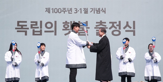 문재인 대통령이 1일 오전 서울 광화문광장에서 열린 제100주년 3.1절 기념식을 마친 뒤 독립영웅 임우철 지사에게 받은 독립의 횃불을 독립의 횃불 청년 단장에게 전달하고 있다. 연합뉴스