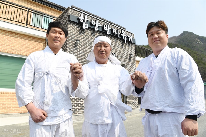 19일 오전 경남 함양군 서하면 송계리 함양방짜유기촌 앞에서 경남도무형문화재 제44호 함양방짜유기장 이점식(가운데) 장인과 그에게 기술을 전수받고 있는 큰 아들 창훈(맨 오른쪽)씨, 작은 아들 상운씨가 손을 맞잡고 기념촬영을 하고 있다. 함양=전혜원 기자