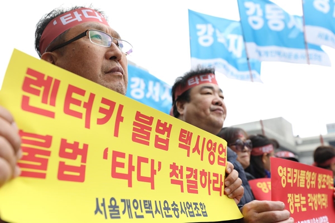 21일 오후 서울 종로구 광화문광장에서 서울개인택시운송사업조합이 주최한 '고 임정남 택시기사 추모 및 3.7 카풀 합의 거부, '타다' 추방 결의대회'에서 택시업계 관계자들이 '타다'를 비판하는 내용의 문구가 적힌 손피켓을 들고 있다. 뉴시스