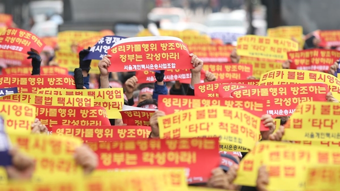 21일 오후 서울 종로구 광화문광장에서 서울개인택시운송사업조합이 주최한 '고 임정남 택시기사 추모 및 3.7 카풀 합의 거부, '타다' 추방 결의대회'에서 택시업계 관계자들이 '타다'를 비판하는 내용의 문구가 적힌 손피켓을 들고 있다. 뉴시스