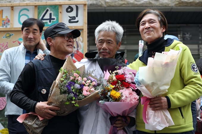 콜텍 노사 조인식이 열린 23일 서울 강서구 콜텍 본사 앞 기자회견에서 이인근(오른쪽부터) 금속노조 콜텍 지회장, 42일간 단식한 임재춘 조합원, 올해 60세로 정년을 맞이하는 김경봉 조합원이 꽃다발을 든 채 환하게 웃고 있다. 연합뉴스