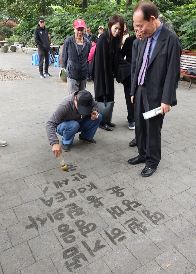 29일 '훙커우 의거' 현장인 중국 상하이 루쉰공원에서 윤 의사의 조카인 윤주 매헌윤봉길의사기념사업회 부회장(오른쪽)이 윤봉길 의사를 기리는 한글 문구를 바닥에 쓰는 중국인 자오청셴씨를 바라보고 있다. 연합뉴스