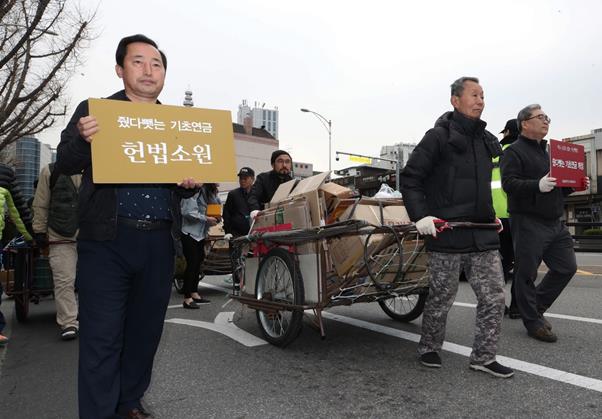 빈곤노인기초연금연대 회원과 노인들이 3월 25일 오전 서울 종로구 경복궁역에서 기초생활수급 노인들의 기초연금 박탈 문제 해결을 요구하며 폐지를 실은 손수레를 끌고 청와대까지 행진하고 있다. 연합뉴스