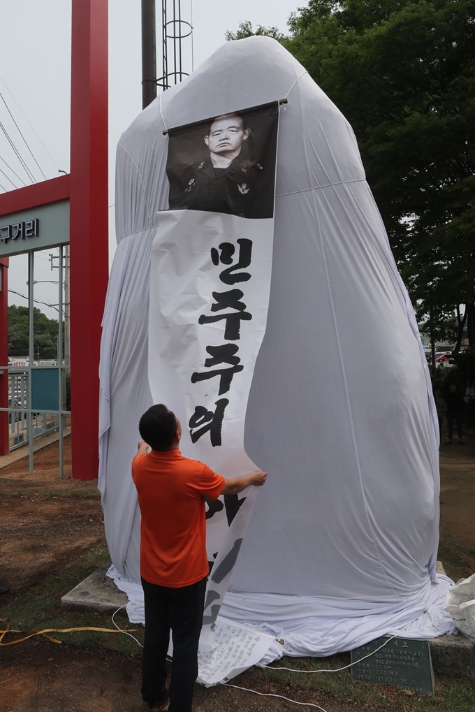 5·18 광주민주화운동 기념일을 하루 앞둔 17일 경기도 포천시 소흘읍 국도 43호선 축석고개에서 민중당 포천시 지역위원회 당원들이 호국로 기념비를 흰 천으로 둘러싸고 있다. 연합뉴스