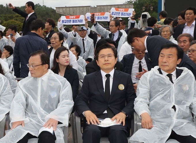 18일 오전 광주 국립5ㆍ18민주묘지에서 열린 5ㆍ18 민주화운동 기념식에 이해찬(왼쪽) 더불어민주당 대표(왼쪽부터), 황교안(가운데) 자유한국당 대표, 손학규 바른미래당 대표가 참석하고 있다. 그 뒤로 황교안 대표의 참석을 반대하는 시민들의 모습이 보인다. 연합뉴스