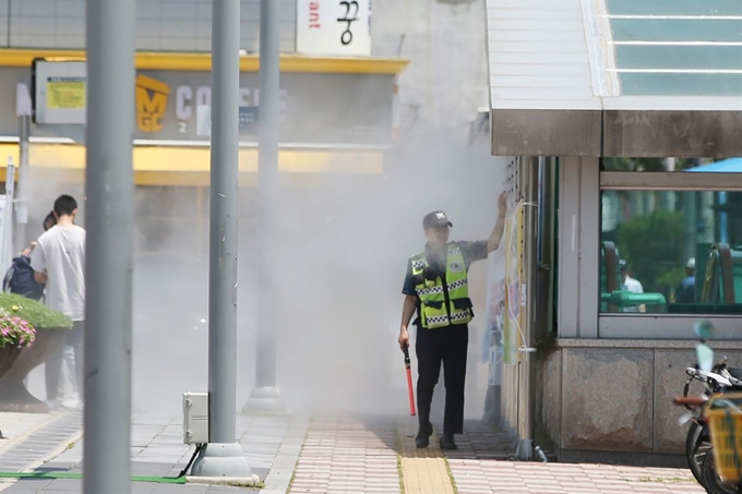 폭염주의보가 내려진 5일 광주 광산구 KTX송정역 광장에서 2019세계수영선수권대회를 앞두고 경계 근무를 하고 있는 경찰관이 열섬 저감 장치(쿨링 포그) 앞에서 열을 식히고 있다. 연합뉴스