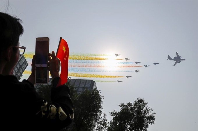 중국 베이징에서 1일(현지시간) 건국 70주년 축하 군사퍼레이드가 열리고 있는 가운데 한 시민이 휴대폰을 이용해 화려한 색깔의 연기를 뿝으며 축하비행중인 중국공군 군용기를 촬영하고 있다. AP 연합뉴스