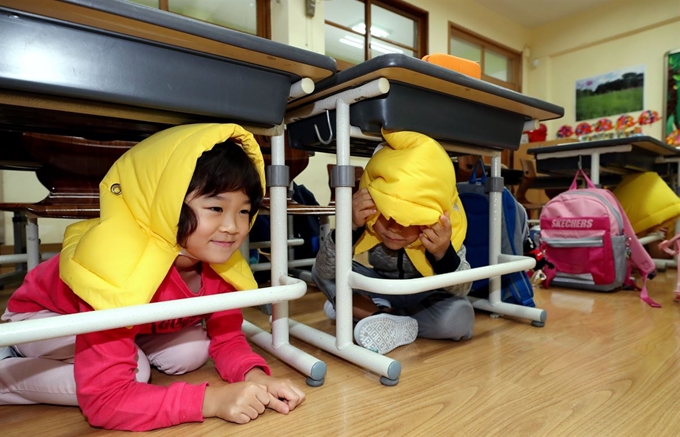 지난 2일 서울 중랑구 신내초등학교에서 열린 2019 재난대응 안전한국훈련 및 긴급구조종합훈련에서 학생들이 방재 모자를 쓰고 책상 밑으로 몸을 피하고 있다. 이날 훈련은 신내초등학교에서 지진으로 인한 도서실 일부 붕괴 및 여진으로 인한 화재 발생 상황을 가정해 진행됐다. 뉴스1