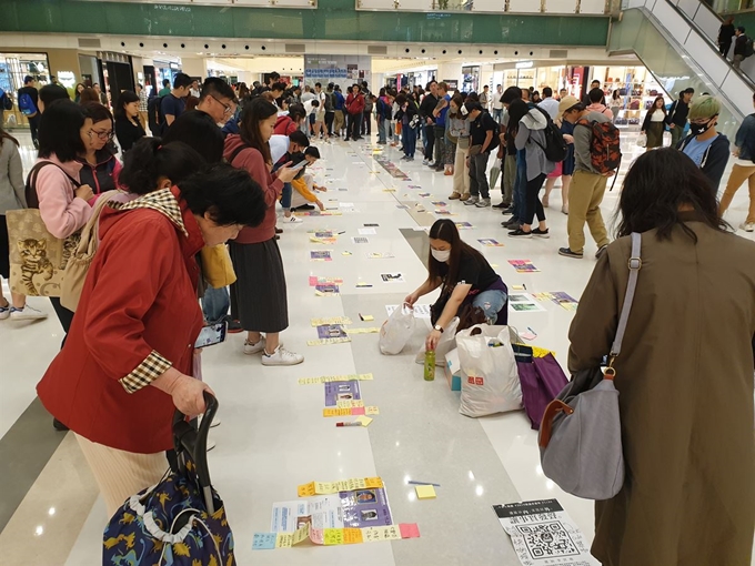 구의원 선거를 사흘 앞두고 21일 저녁 카오룽반도 샤틴 지하철역 쇼핑몰에서 벌어지고 있는 홍콩판 낙선 운동. 바닥에 붙어있는 사틴의 41개 전체 지역구 출마 후보 사진과 그 옆에 지지, 반대 의사를 적어 놓은 포스트잇을 들여다보고 있다. 김광수 특파원