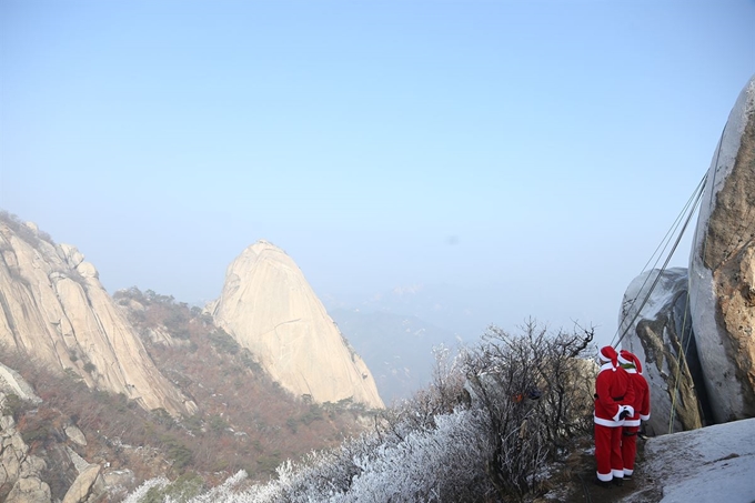 22일 서울 북한산 만경대에서 산타클로스 복장을 한 쌩곰산악회와 멀티암벽산악회 대원들이 안전산행 기원과 다가오는 크리스마스를 기념하는 퍼포먼스를 벌이기 앞서 백운대와 인수봉을 바라보고 있다. 연합뉴스