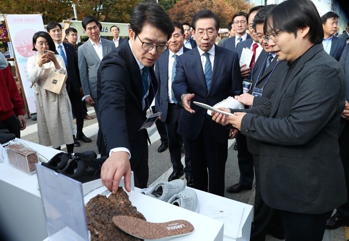 지난 10월 30일 서울 성동구 서울숲 언더스탠드애비뉴 일대에서 열린 제3회 '서울숲 청년소셜벤처 엑스포'가 행사 중 정원오(왼쪽) 성동구청장과 박원순(가운데) 서울시장 등이 '비즈니스 가지장터' 행사를 주관한 임팩트스퀘어 도현명(오른쪽) 대표로부터 소셜벤처기업 'LAR' 제품에 대한 설명을 듣고 있다. '서울숲 청년소셜벤처 엑스포'는 기초자치단체가 주관하는 전국 유일의 소셜벤처 엑스포다. 성동구 제공/2019-12-21(한국일보)