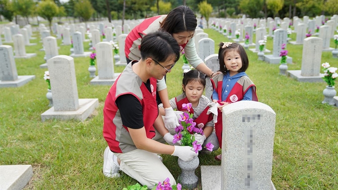 롯데건설 직원과 가족이 국립 서울현충원에서 묘비 정비 봉사활동을 하고 있다. 롯데건설 제공