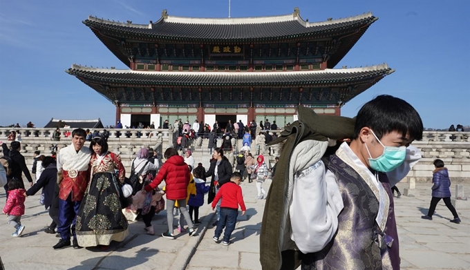 설 연휴 사흘째이자 국내에서 세 번째 우한 폐렴 확진 환자가 발생한 26일 서울 경복궁에서 마스크를 쓴 관광객이 기념 촬영 후 옷을 입고 있다. 연합뉴스