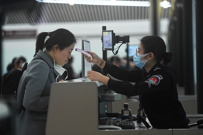 중국 우한에서 발생한 신종 코로나바이러스가 세계 각국으로 급속히 확산되는 가운데 26일 중국 충칭 장베이국제공항에서 검역 직원이 승객의 체온을 재고 있다. 충칭=로이터 연합뉴스