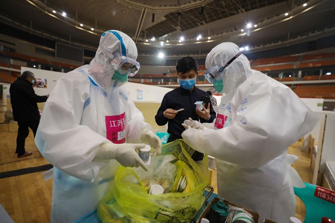 신종 코로나바이러스 감염증 경증환자를 위한 임시병원 역할을 하고 있는 중국 후베이성 우한의 스포츠센터에서 5일 방호복을 입은 간호사들이 환자들에게 간식을 나눠주고 있다. 우한=AFP 연합뉴스