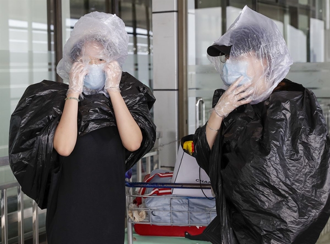 마스크를 쓴 관광객들이 18일 필리핀 마닐라 국제공항 출국장에서 항공편을 기다리는 동안 쓰레기 봉지와 작은 비닐봉지로 머리와 몸을 가리고 있다. 마닐라=AP 뉴시스