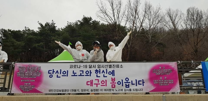 권봉기 국민건강보험공단 과장(사진 가운데)이 대구 달서구 선별진료소에 봉사활동을 나온 공단 직원들과 함께 제작한 현수막에서 기념촬영을 하고 있다. 국민건강보험공단 제공