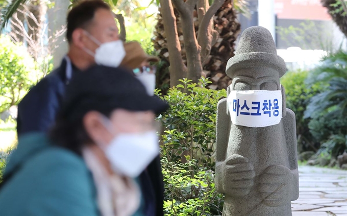 28일 오전 제주국제공항에서 관광객들이 마스크가 씌워진 돌하르방 앞을 지나가고 있다.제주도는 18만명의 관광객이 몰리는 황금연휴에 코로나19 경각심을 일깨우기 위해 도내 돌하르방 약 40개에 마스크를 씌울 방침이다. 뉴스1