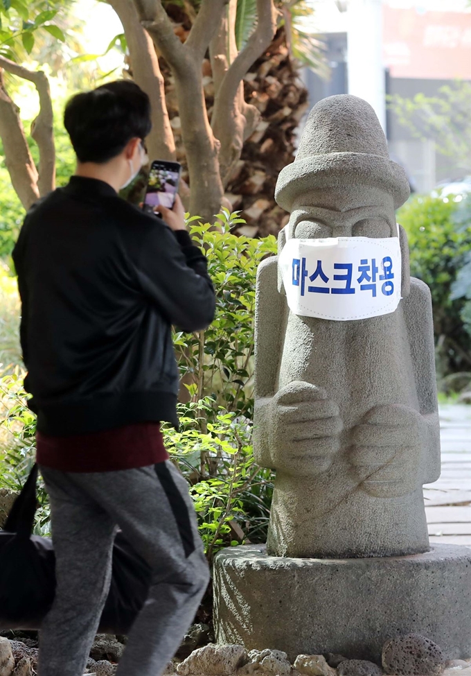 28일 오전 제주국제공항에서 관광객들이 마스크가 씌워진 돌하르방 앞을 지나가고 있다.제주도는 18만명의 관광객이 몰리는 황금연휴에 코로나19 경각심을 일깨우기 위해 도내 돌하르방 약 40개에 마스크를 씌울 방침이다. 뉴스1