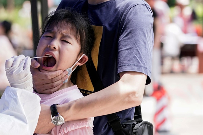 중국 후베이성 우한에서 16일 코로나19 핵산검사를 위해 의료진이 검체를 채취하는 동안 아이가 부모의 손에 붙들려 괴로운 표정을 짓고 있다. 우한=로이터 연합뉴스