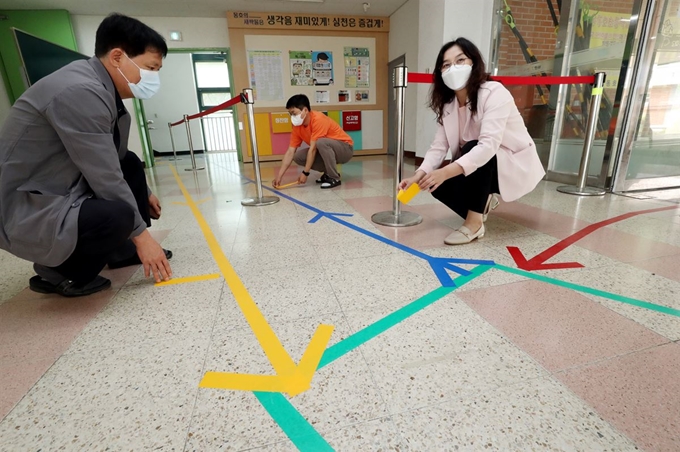 25일 서울 성동구 동호초등학교에서 교직원들이 아이들의 등교를 준비하며 체온 측정 등을 마친 아이들과 아닌 아이들이 섞이지 않도록 등교 동선을 색 테이프로 표시하고 있다. 연합뉴스