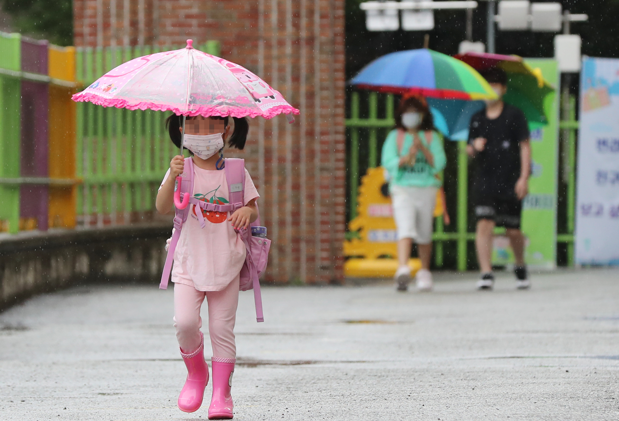 광주·전남지역에 비가 내린 18일 오전 광주 북구 오치초등학교·병설유치원에서 학생들이 마스크를 쓰고 우산을 든 채 발열 체크하기 위해 이동하고 있다.연합뉴스