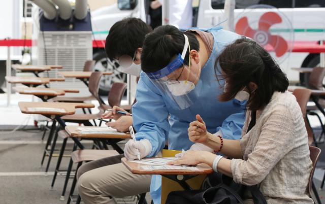 코로나19 검사 대상자들이 13일 서울 강남구 보건소에 마련된 선별진료소에서 의료진을 도움을 받아 검사 전 문진표를 작성하고 있다. 뉴시스