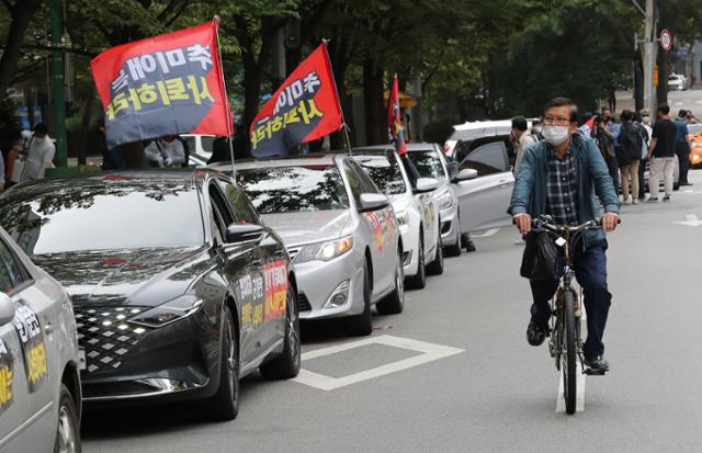 3일 오후 서울 강동구민회관 인근에서 진행된 보수단체 새로운한국을위한국민운동(새한국) 주최 개천절 차량집회에 참여한 차량 옆으로 한 시민이 자전거를 타고 지나가고 있다. 뉴시스