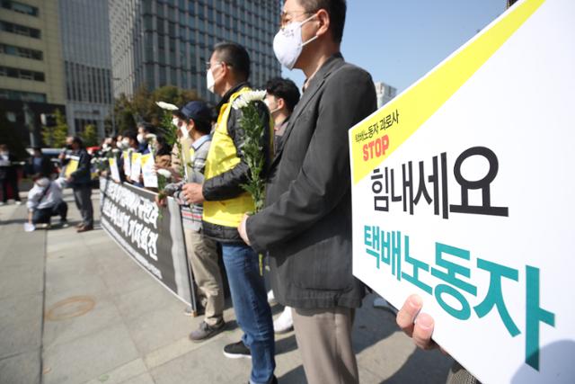 19일 서울 광화문광장 이순신 동상 앞에서 열린 '대기업 택배사 규탄과 택배노동자 과로사 예방 호소하는 택배 소비자 기자회견'에서 참석자들이 손팻말과 국화를 들고 있다. 연합뉴스