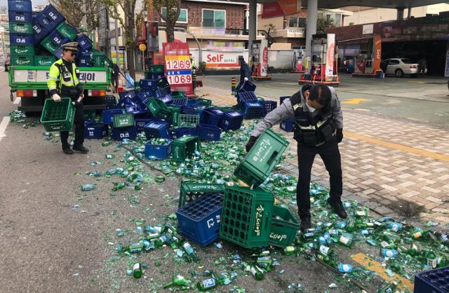 6일 오전 부산 연제구 한 도로를 달리던 화물차에 실린 소주 100상자가 도로에 떨어져 출동한 경찰관이 깨진 소주병을 정리하고 있다. 부산경찰청 제공·