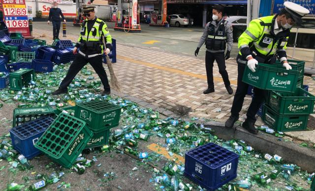 6일 오전 부산 연제구 한 도로를 달리던 화물차에 실린 소주 100상자가 도로에 떨어져 출동한 경찰관이 깨진 소주병을 정리하고 있다. 부산경찰청 제공