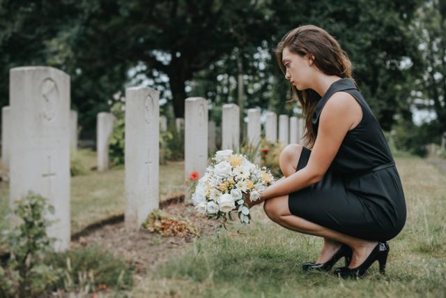 Young widow laying flowers at the grave