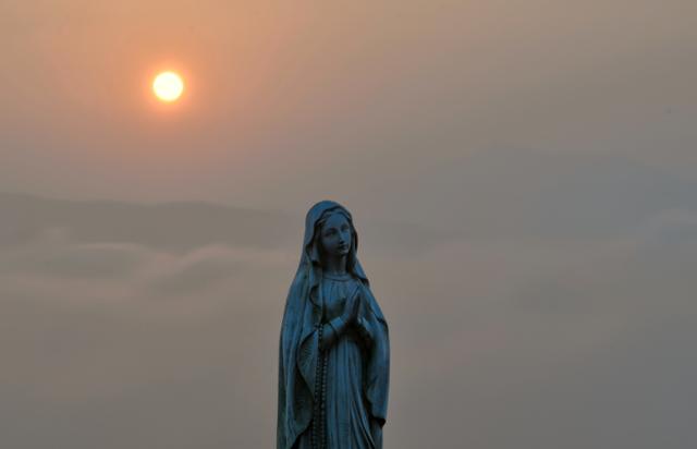 산 정상에 있는 성모마리아상 뒤로 태양이 솟고 있다.