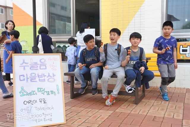 제주 제주시 삼화2차부영아파트 관리동 1층에 자리한 수눌음육아나눔터 1호점에서 진행된 ‘수눌음 마을밥상’을 찾은 아이들이 무료로 제공된 떡꼬치를 맛있게 먹고 있다. 안내판에는 ‘수늘음’으로 잘못 표기돼 있다. 한국일보 자료사진