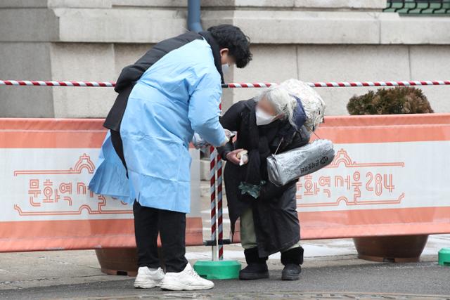 16일 오전 서울역 광장에서 코로나19 임시선별검사소 관계자가 한 노숙인에게 핫팩과 간식을 전달하고 있다. 83세의 이 노숙인은 '지금은 가진 먹을거리가 많아 사양하던 중 이였다'며, '도움 준 사람들 모두 갓 블레스유(God bless you)'라고 전했다. 연합뉴스