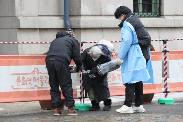 16일 오전 서울역 광장에서 코로나19 임시선별검사소 관계자와 노숙인이 핫팩과 간식을 노년의 노숙인(가운데)에게 전달하고 있다. 83세의 이 노숙인은 '지금은 가진 먹을거리가 많아 사양하던 중 이였다'며, '도움 준 사람들 모두 갓 블레스유(God bless you)'라고 전했다. 연합뉴스