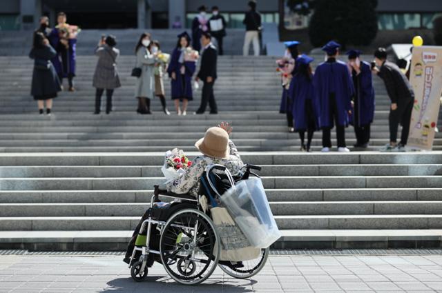 26일 서울 관악구 서울대학교 중앙도서관 앞에서 한 할머니가 휠체어에 앉아 학사모를 쓰고 다른 가족들과 함께 기념촬영을 하는 손녀의 모습을 바라보며 손을 흔들어 인사하고 있다. 신종 코로나바이러스 감염증(코로나19) 확산으로 이날 학위수여식은 온라인 실시간 재생 방식으로 열렸다. 연합뉴스