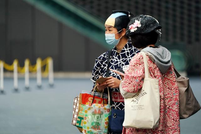 지난 6일 일본 도쿄에서 전통복장을 입은 시민이 마스크를 쓰고 일행과 함께 길을 가고 있다. 도쿄도는 12일부터 '만연방지 등 중점조치'가 적용된다. 도쿄=AP 뉴시스