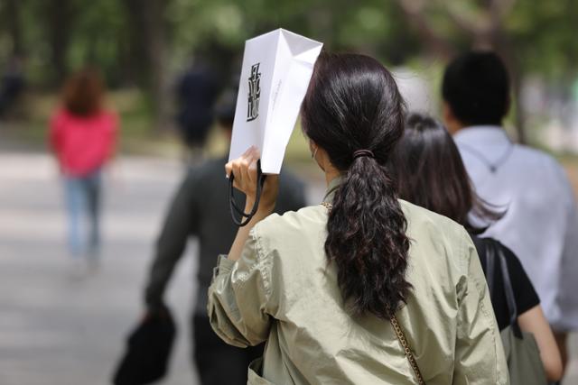 낮 기온이 27도까지 올라가며 여름 날씨를 보인 22일 정오를 넘긴 시간 서울 여의도공원에서 시민이 쇼핑백으로 햇빛을 가리고 있다. 연합뉴스