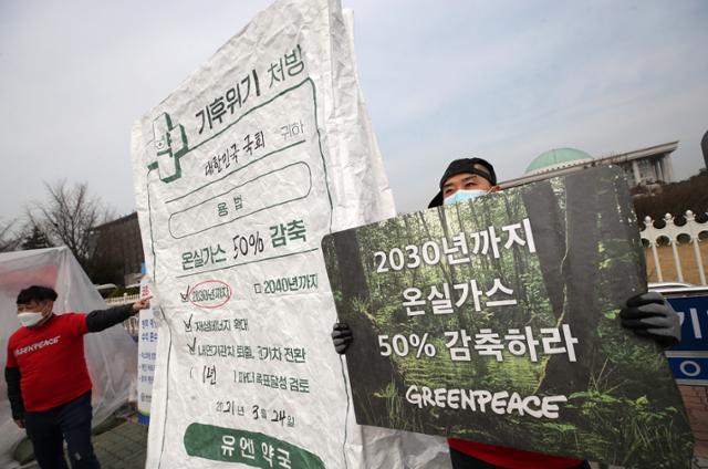 국제환경단체 그린피스 활동가들이 3월 국회의사당 앞에서 온실가스 감축을 촉구하며 '기후위기 처방, 유엔 약국'이라고 적힌 초대형 약 봉투를 국회에 전달하는 퍼포먼스를 하고 있다. 뉴스1