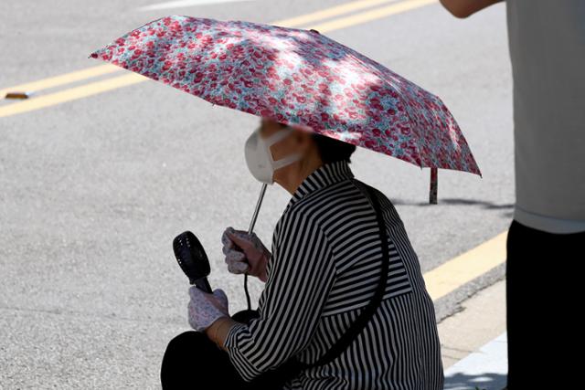 폭염이 이어지는 18일 오전 서울 강서구 임시선별검사소에서 한 시민이 양산과 손 선풍기로 더위를 식히고 있다. 뉴시스